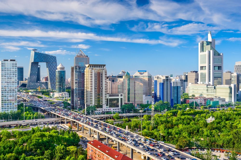 Beijing cityscape with modern skyscrapers, lush greenery, and a busy highway under a vibrant blue sky.