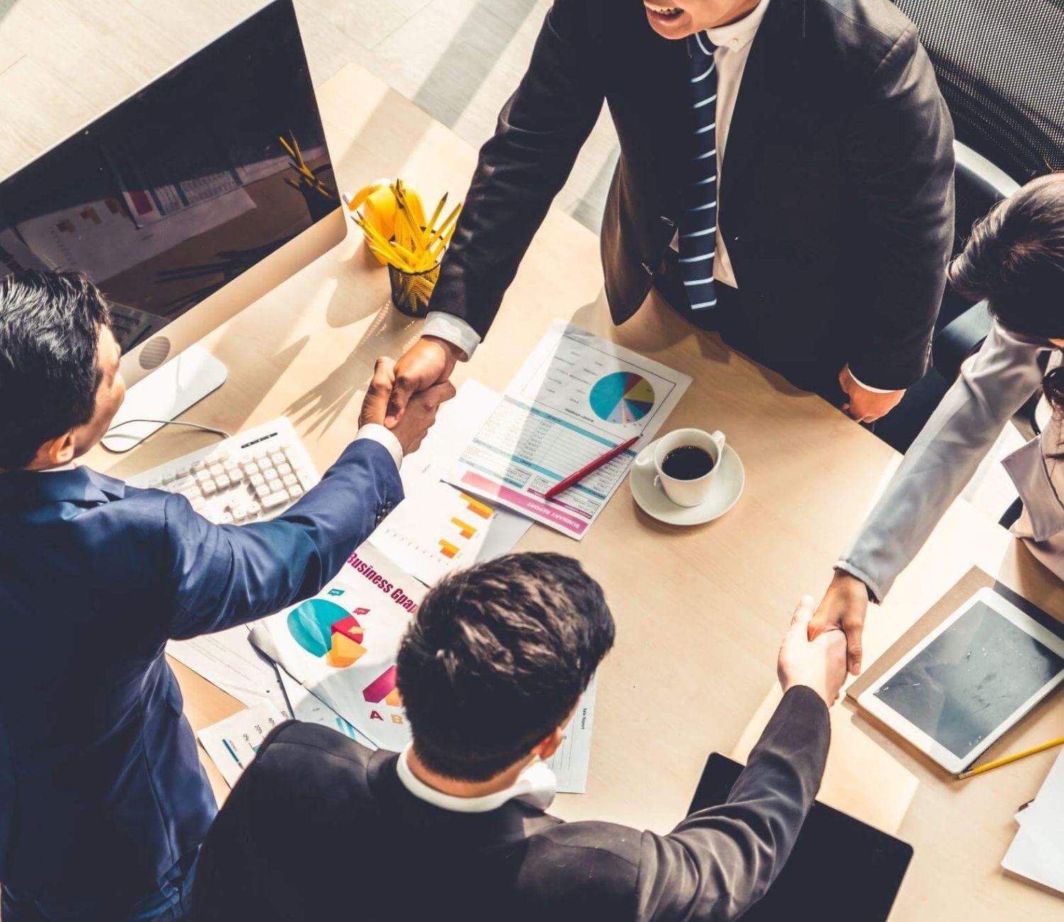 Business meeting with diverse professionals shaking hands over charts, reflecting collaboration and success.