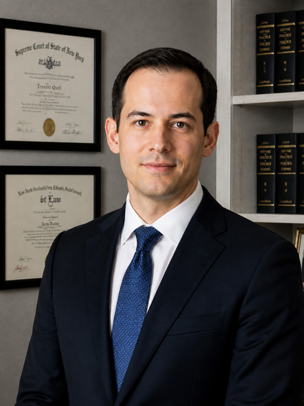A person in a suit in an office setting, with a confident expression, facing forward.